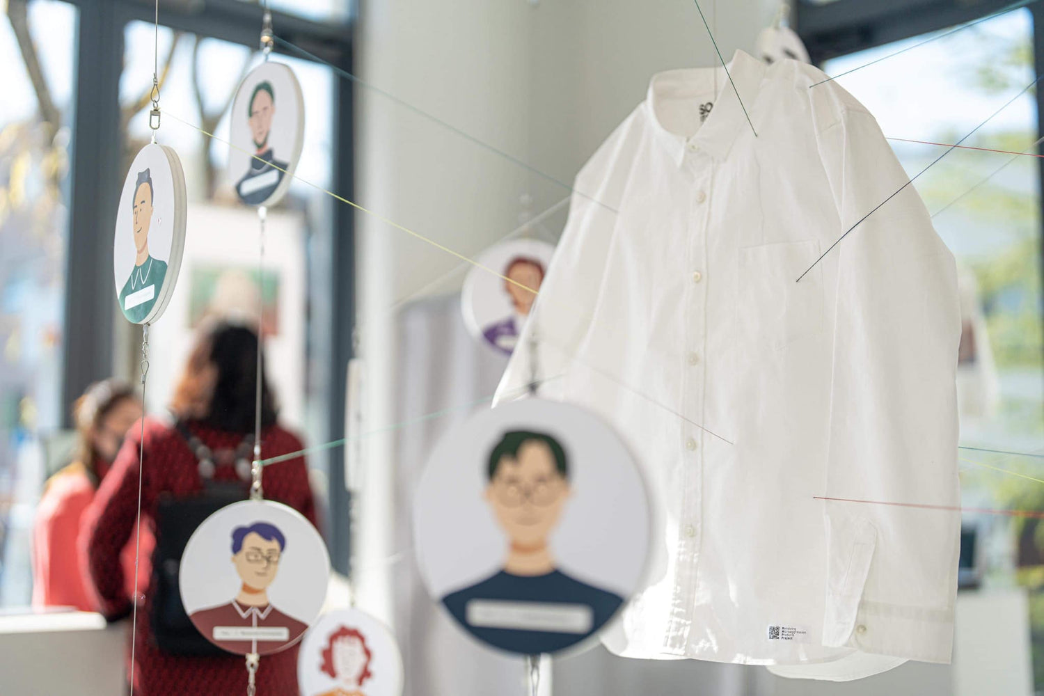 吊り下げられた服に対して、周辺に生産者の顔がイラスト化されたものが浮いている。
